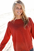 Portrait of blonde woman wearing orange top standing on beach, smiling