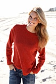 blonde Frau in orangefarbenem Pulli und Jeans am Strand