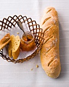 Slices of baguette and jam jar in wicker basket beside baguette