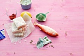 Whole and fillets of frozen fish with ingredients on pink background