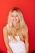 Portrait of happy woman with long blonde hair laughing and standing against red background