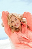 Portrait of beautiful blonde woman wearing peach sweater sitting and smiling