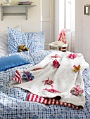 Red and white plaid blanket with fabric flowers on bed with linen bed sheet