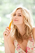Beautiful woman wearing summer dress holding carrot and smiling