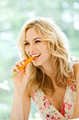 Pretty blonde woman wearing summer dress eating carrot