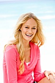 Portrait of happy blonde woman wearing pink sweater, laughing on beach