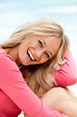 Close-up of happy blonde woman wearing pink sweater laughing and leaning on her knee