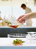 Clear, smoked lamb soup being poured from a glass sauciere into a glass bowl