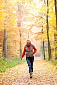 Blonde woman wearing gray puffer jacket walking on dirt track in autumn forest