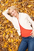 Blonde woman in bright jacket and orange top lying on autumn leaves, overhead view