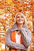 Contemplative blonde woman wearing gray cardigan smiling in autumn forest
