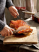 Woman slicing roasted pork with beer sauce on chopping board for winter