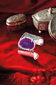Close-up of silver coloured metal bangle with purple flat gemstone on it