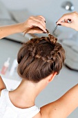 Rear view of brunette woman pinning up her braids while preparing updo