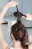 Close-up of dark haired woman back combing her hair with brush while preparing updo