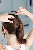 Rear view of woman with dark haired pining up her hair while preparing updo