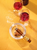 Red wine in cognac glasses and ashtray with lit cigar
