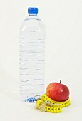 Water bottle and apple with measuring tape symbolizing dieting