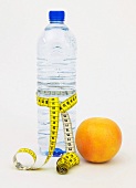 Grapefruit and water bottle with measuring tape symbolizing dieting