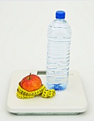 Apple with measuring tape and water bottle on weighing scale, Icon image for diet