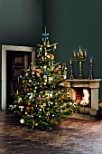 Christmas tree with decoration besides fire place and candle stand