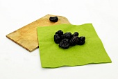 Dry plums on green cloth with wooden platter on white background