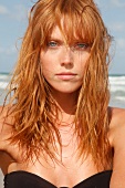 Rothaarige Frau mit Sommersprossen im schwarzen Bikini am Strand am Meer