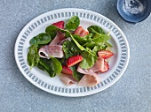 Spinach salad with strawberries and ham on plate