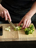 Close-up of hand cutting broccoli on chopping board, step 1
