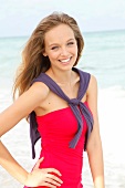 Portrait of beautiful blonde woman wearing red dress standing on beach, smiling