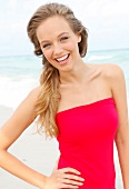 Portrait of beautiful blonde woman wearing red dress standing on beach, smiling