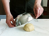Close-up of hand covering dough with bow, step 1