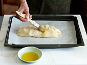 Close-up of hand applying butter on strudel dough in baking dish