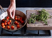 Close-up of hand adding herbs on roasted cherry tomatoes in pan