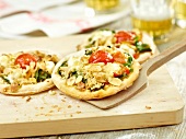 Crumble pizza with spinach and tomatoes on wooden spatula and board