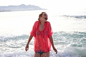 Frau im blauen Bikini, transparente Bluse in pink am Strand im Wasser