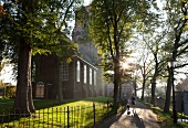 Woman walking with dog on road in front of church in Ransdorp village, Noord, Amsterdam