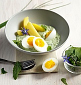 Halved eggs and boiled potatoes with green sauce in bowl 