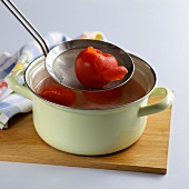 Peeled tomatoes being removed with sieve from casserole, step 2