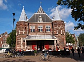 Tourists standing and cycling outside Waag monument in Nieuwmarkt, Amsterdam, Netherlands