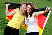 Portrait of two beautiful women holding German flag and smiling
