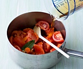 Vegetable broth poured on tomatoes in pan for preparing vegetarian Italian sauce, step 2