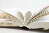 Close-up of open book with pages folded in heart shape on white background