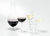 Carafe, shot glass and wine glasses with red and white wine on white background