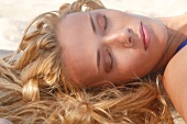 Frau liegt schlafend im Sand am Strand, close-up