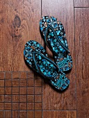 Pair of blue and black thong patterned flip flop on wooden floor
