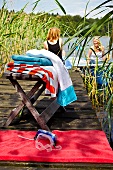 Women at lakeside with reed grass with scuba mask on red towel and on stool