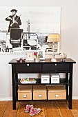 Storage boxes under a black console table against a wall hung with a framed photograph