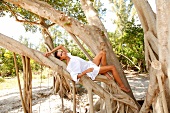 Woman in a white tunic relaxes on a tree