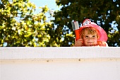 Little boy in fireman costume peeping above the wall